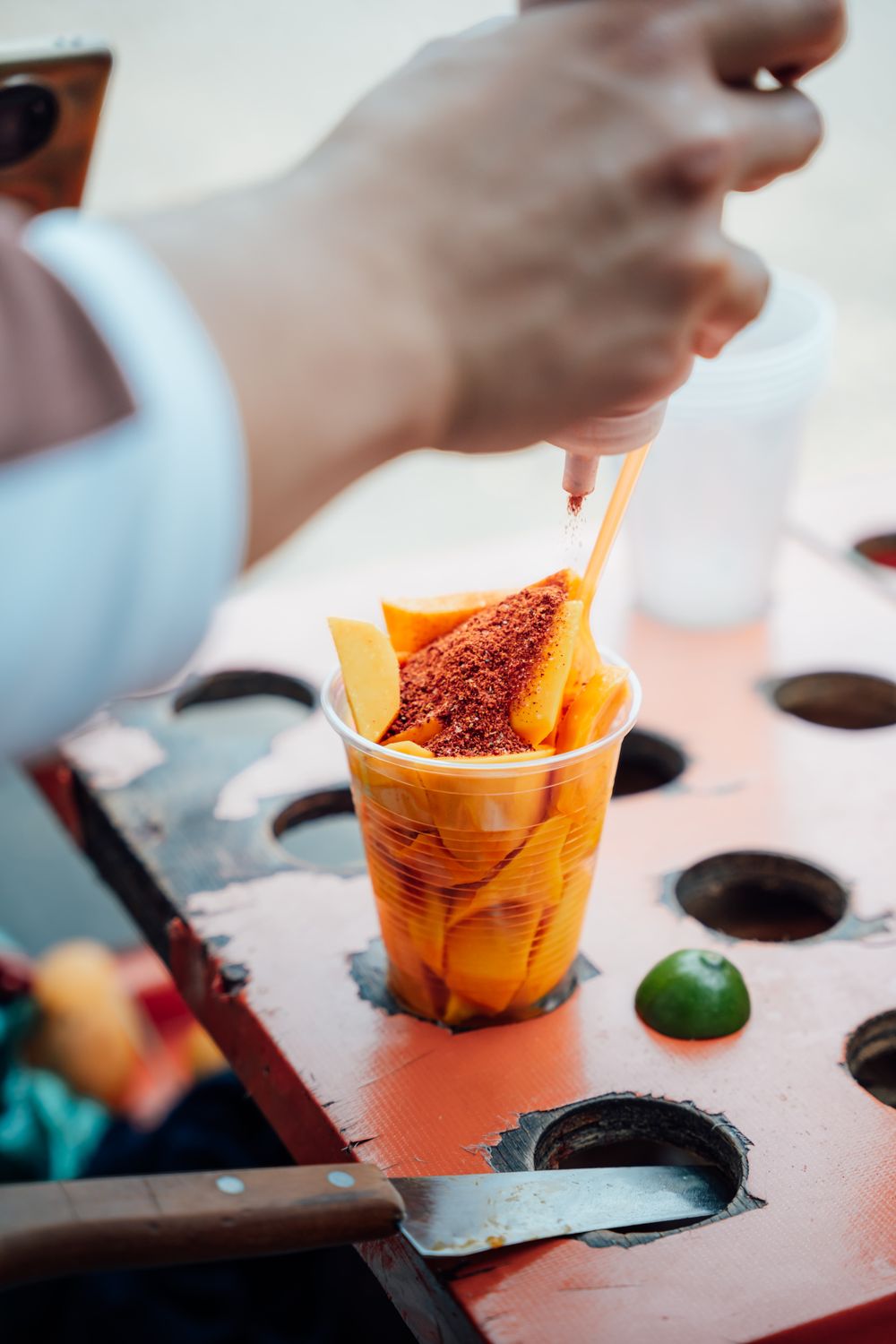 A cup of fresh mango being dusted with chilli powder
