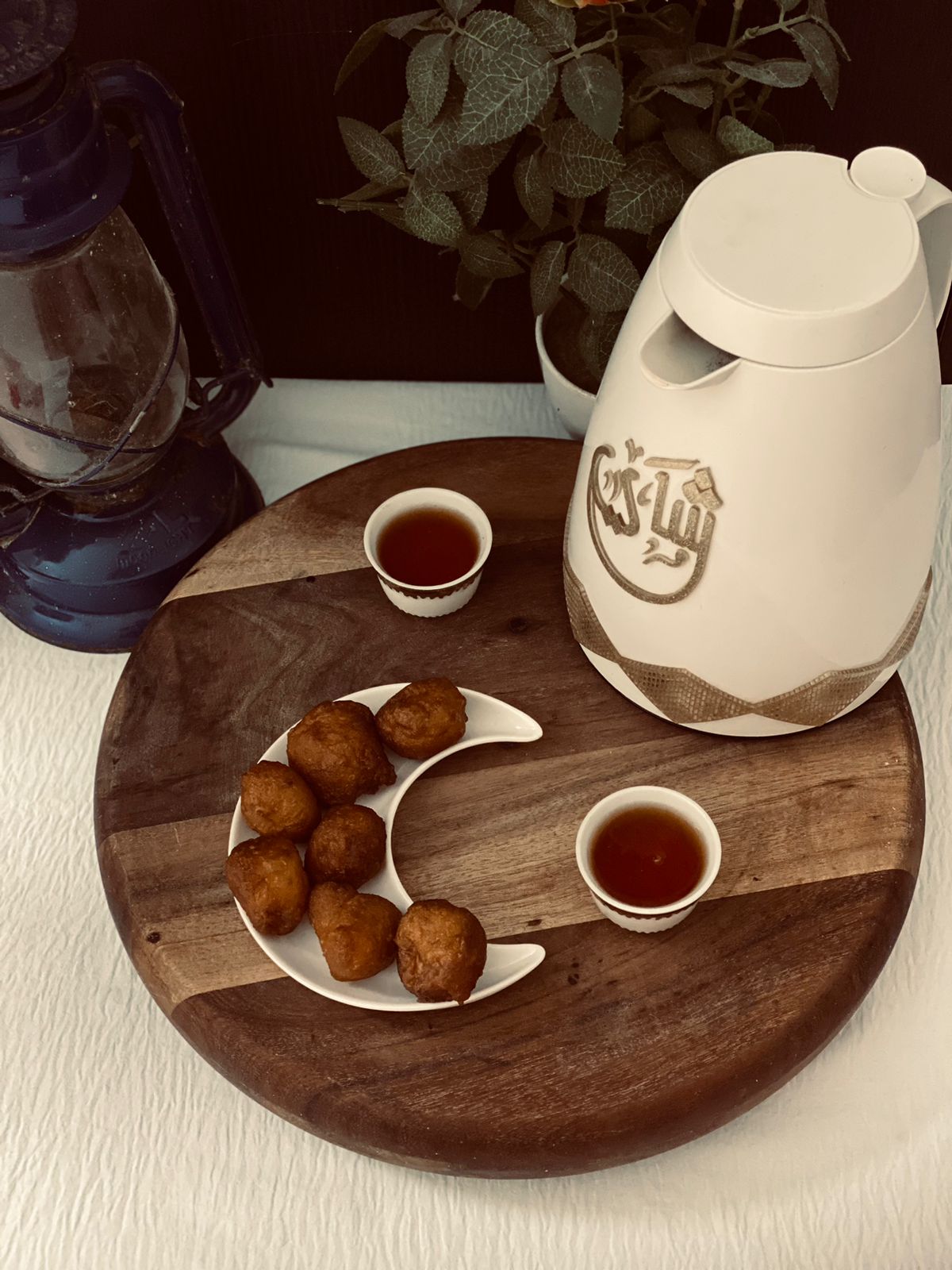Luqaimat on a crescent plate beside cups of Arabic coffee and a dallah