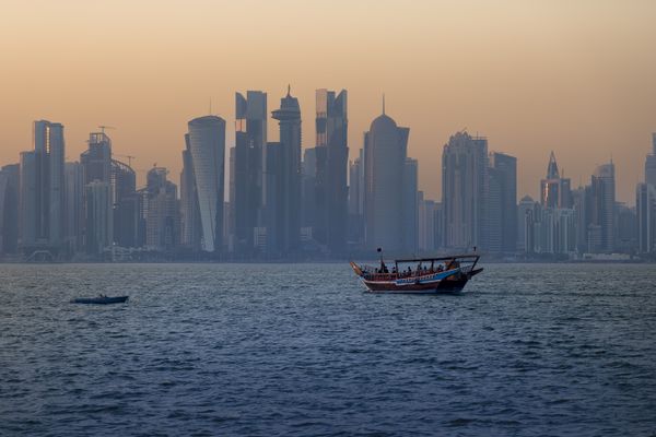 Doha's skyline at sunset with a traditional dhow on the water