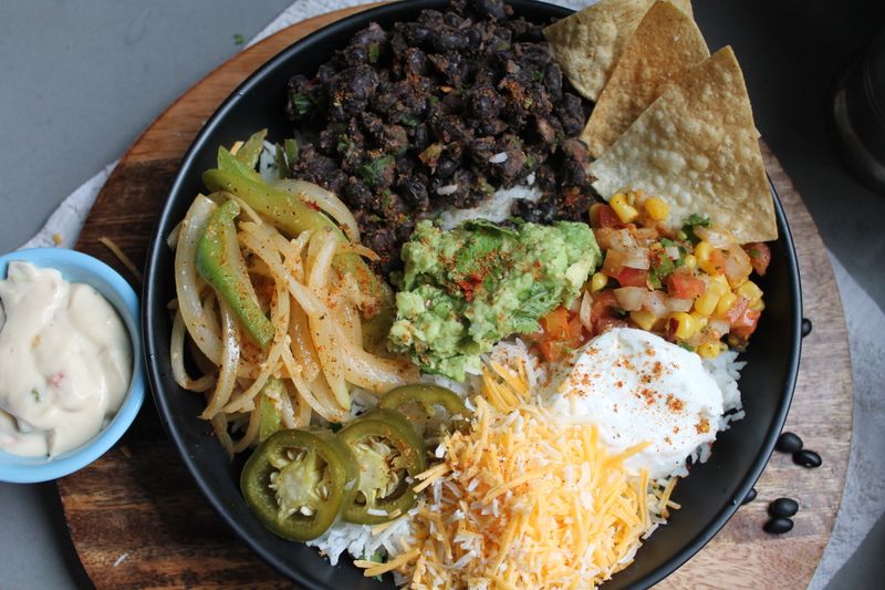 A burrito bowl with guacamole, black beans and shredded cheese